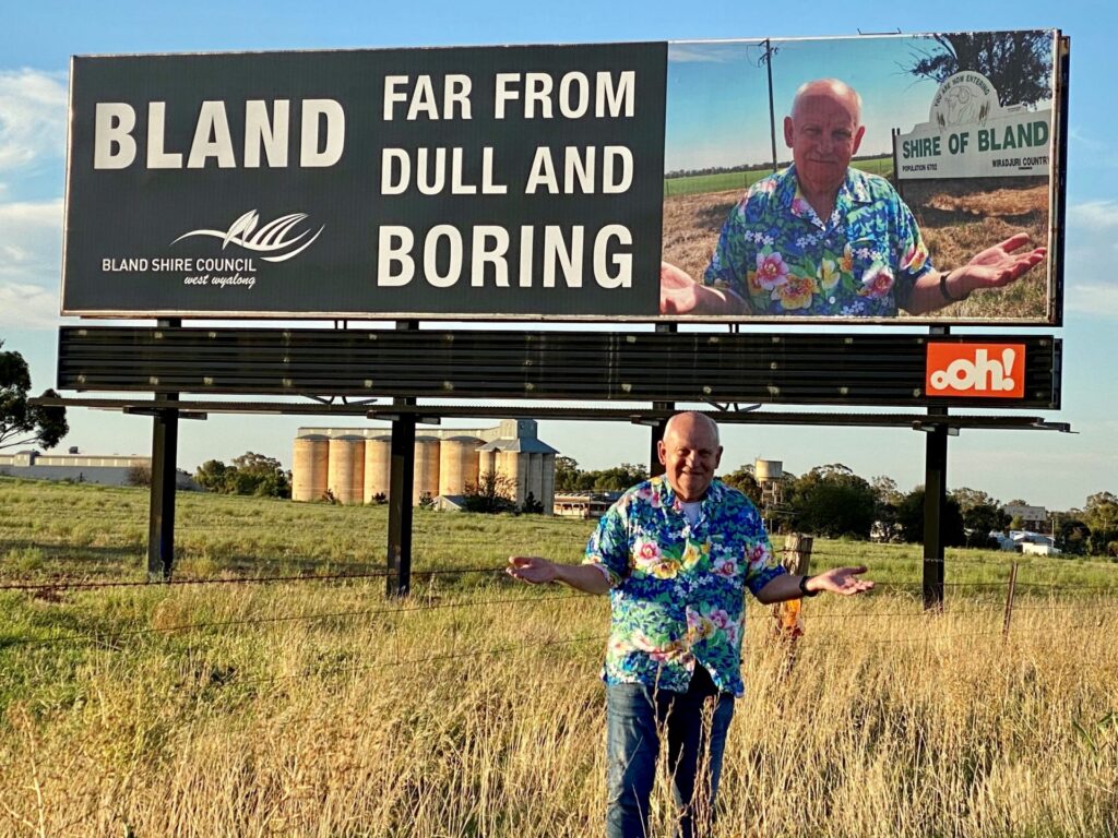 Bland Shire Council's General Manager, Ray Smith, at the the Bland, Dull and Boring billboard on the Newell Highway, Bland Shire, Australia. Image taken by Donna Smith